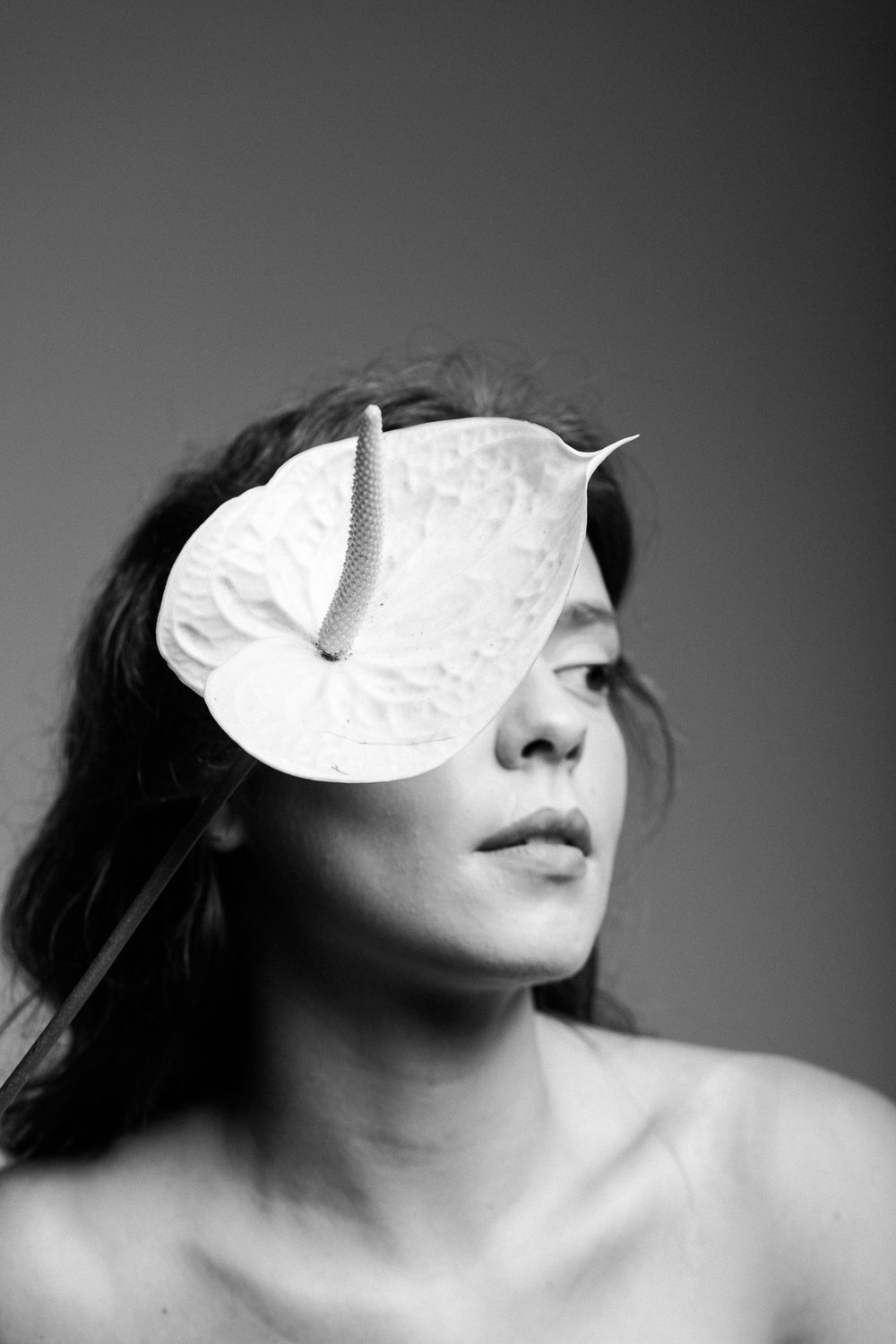 Black and white portrait with a delicate white leaf covering one eye in an artistic composition.