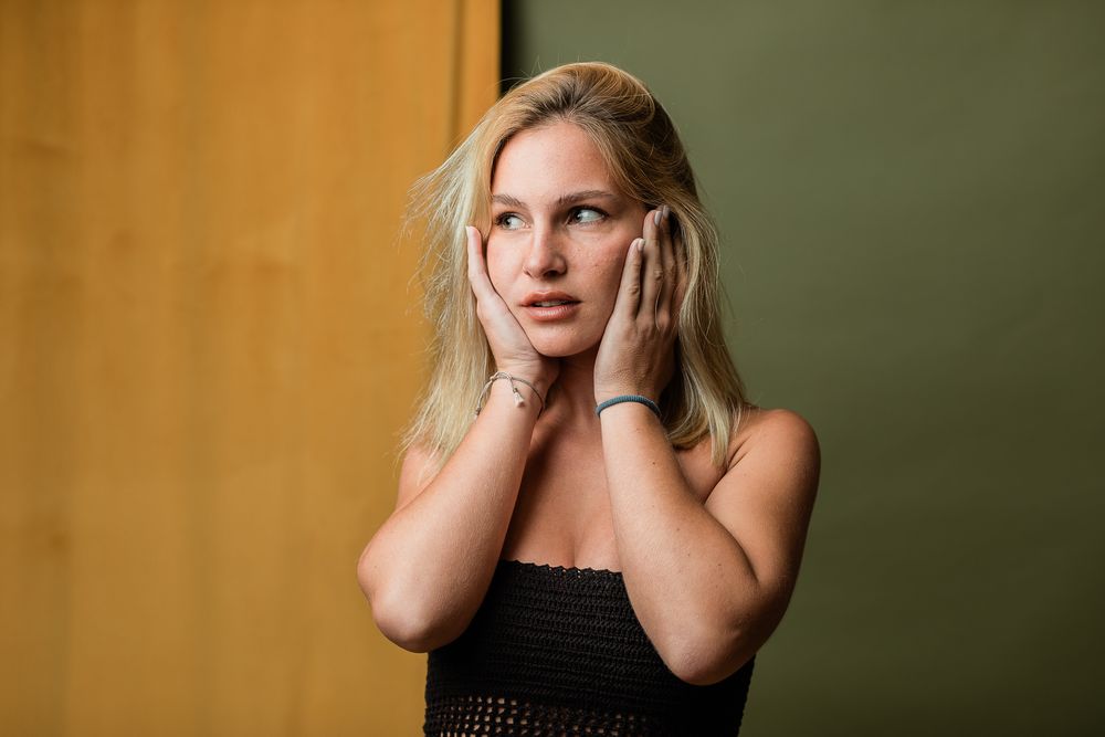 Woman in black top poses in front of warm gold background in professional studio fashion portrait series.