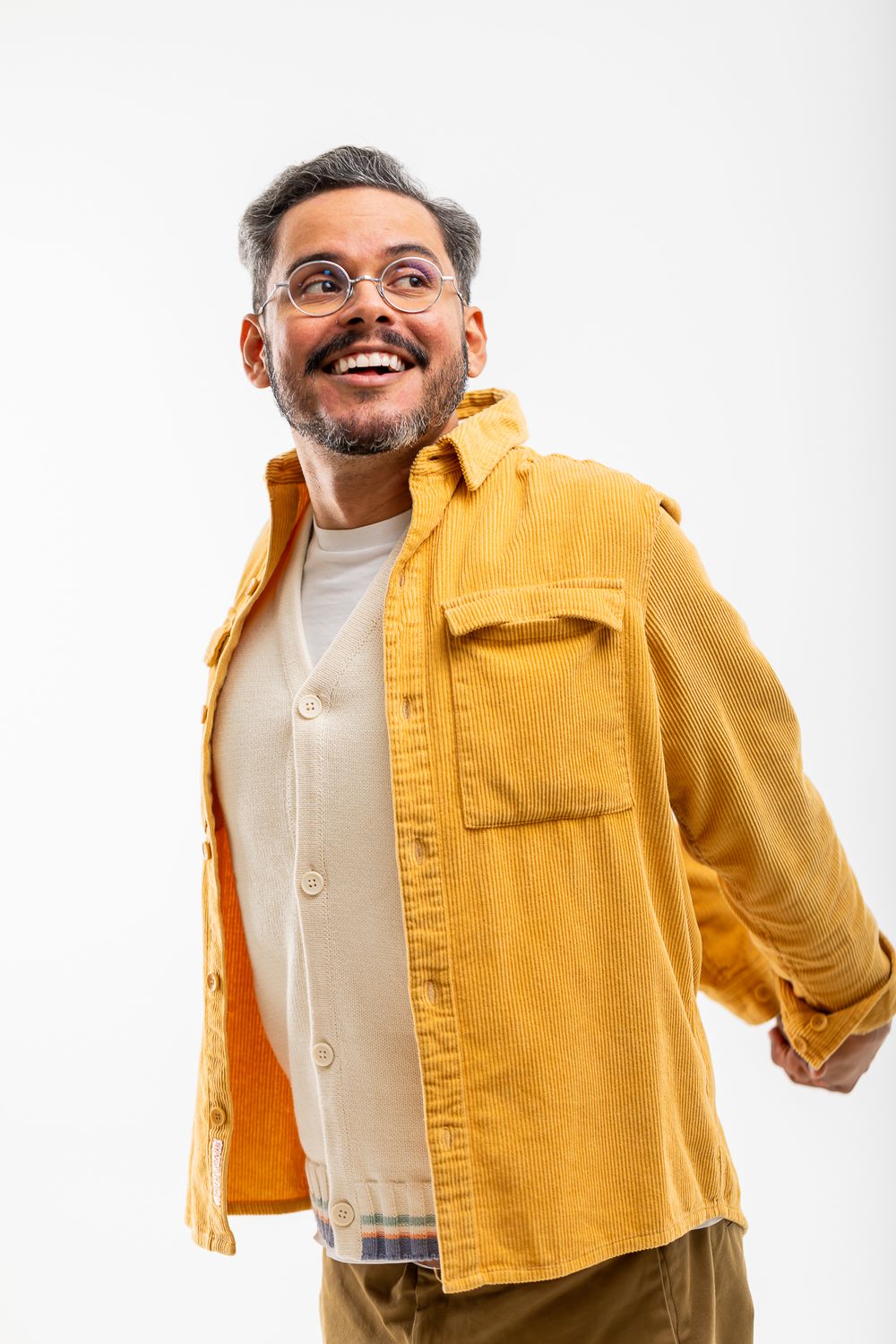 Person wearing glasses and a yellow button-up overshirt smiles warmly while posing against a white background.