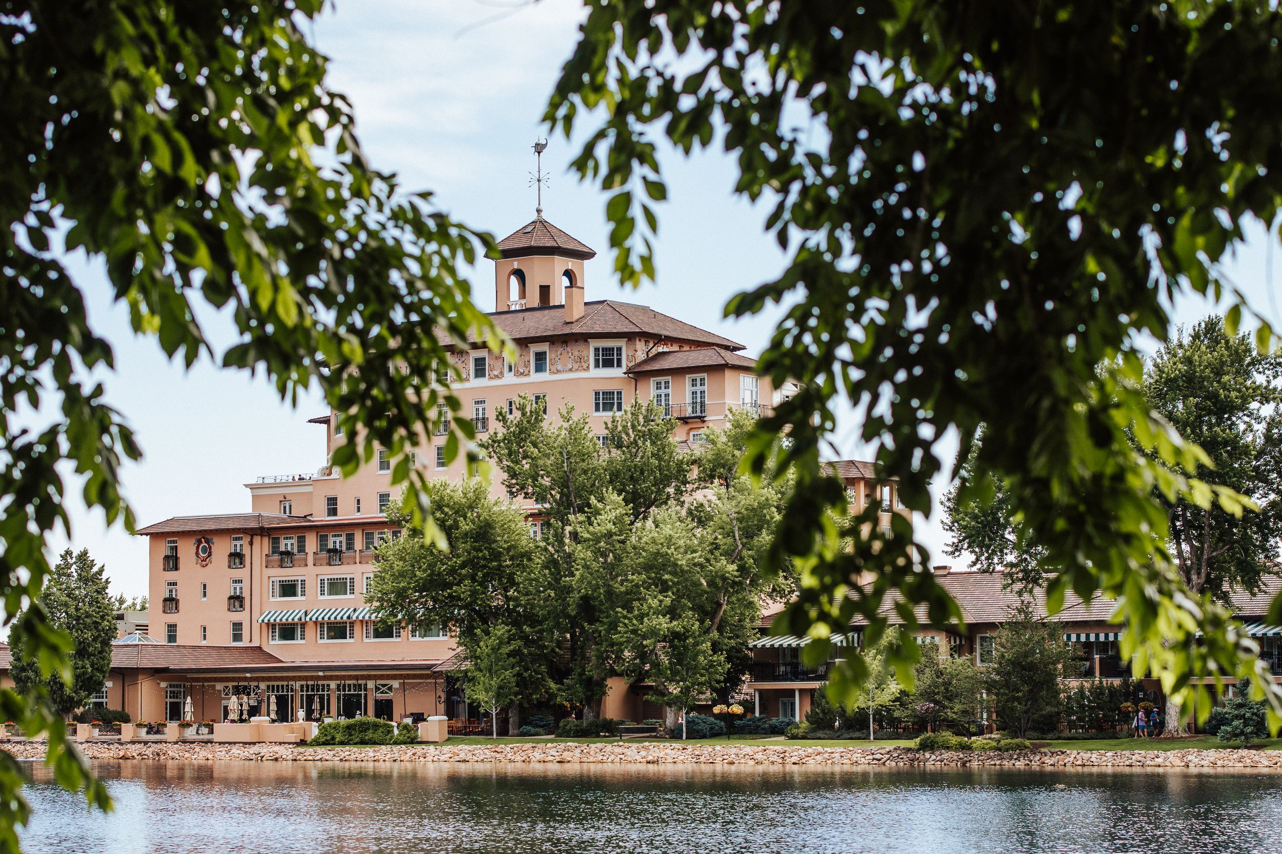 Historic pink Broadmoor Hotel reflects in Cheyenne Lake with trees framing the grand resort in Colorado Springs.