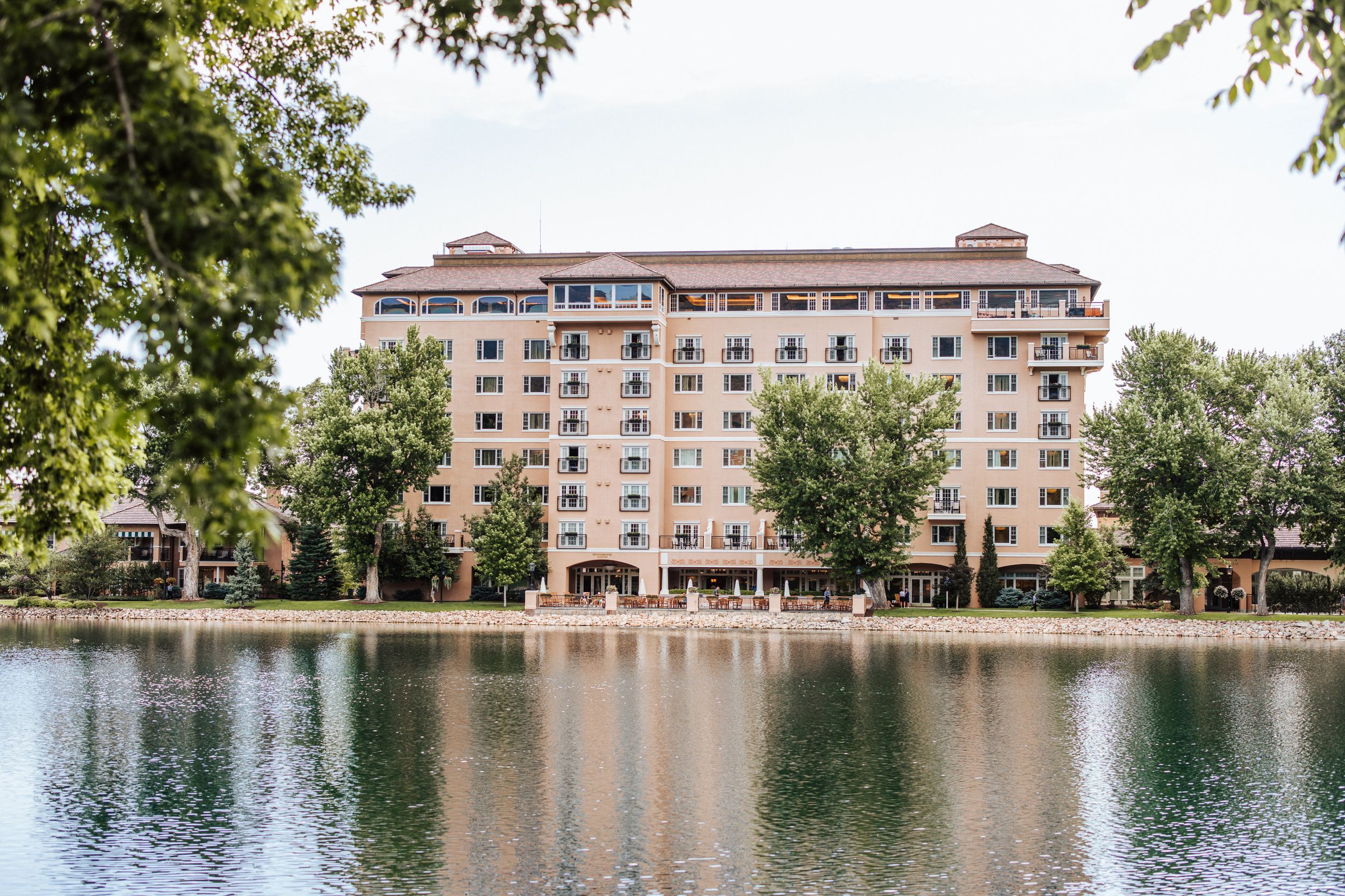 Pink stucco apartment building reflects in calm lake waters surrounded by trees at Lake Hollingsworth in Lakeland, Florida.