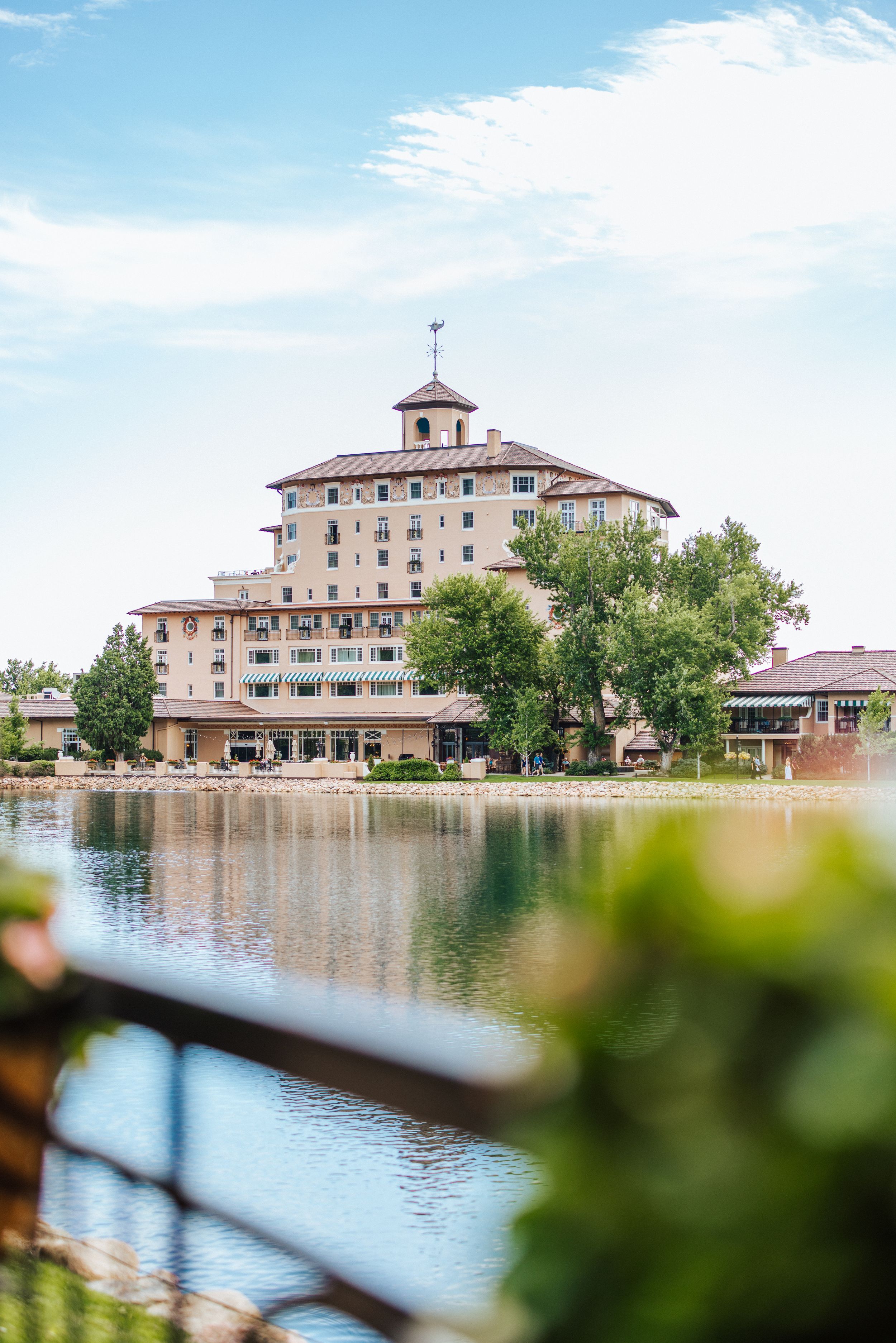 The Broadmoor Hotel stands majestically beside a reflective lake on a sunny day in Colorado Springs.