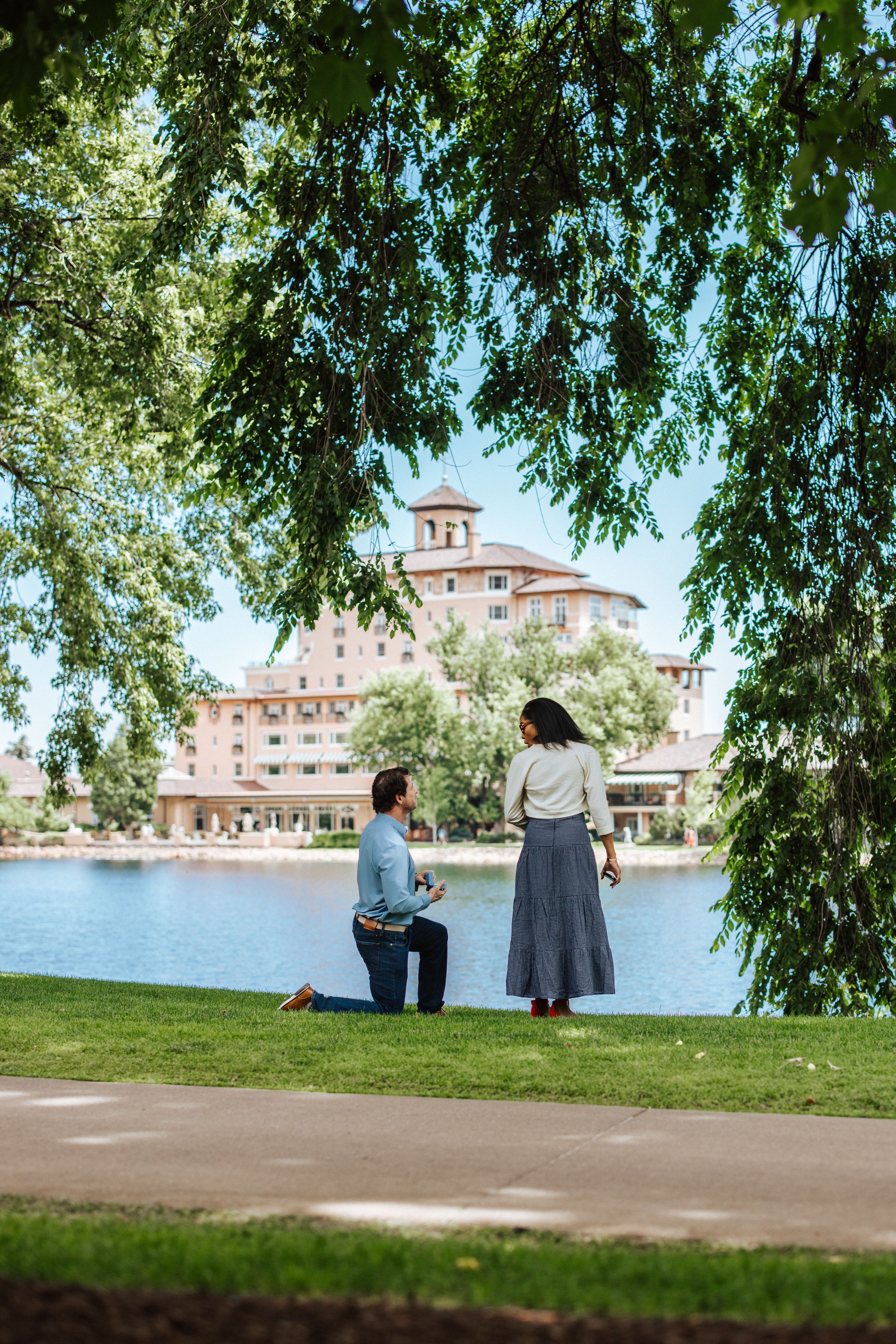 Two people enjoy a peaceful view of the Broadmoor Hotel's iconic buildings across the serene lake on a sunny day.