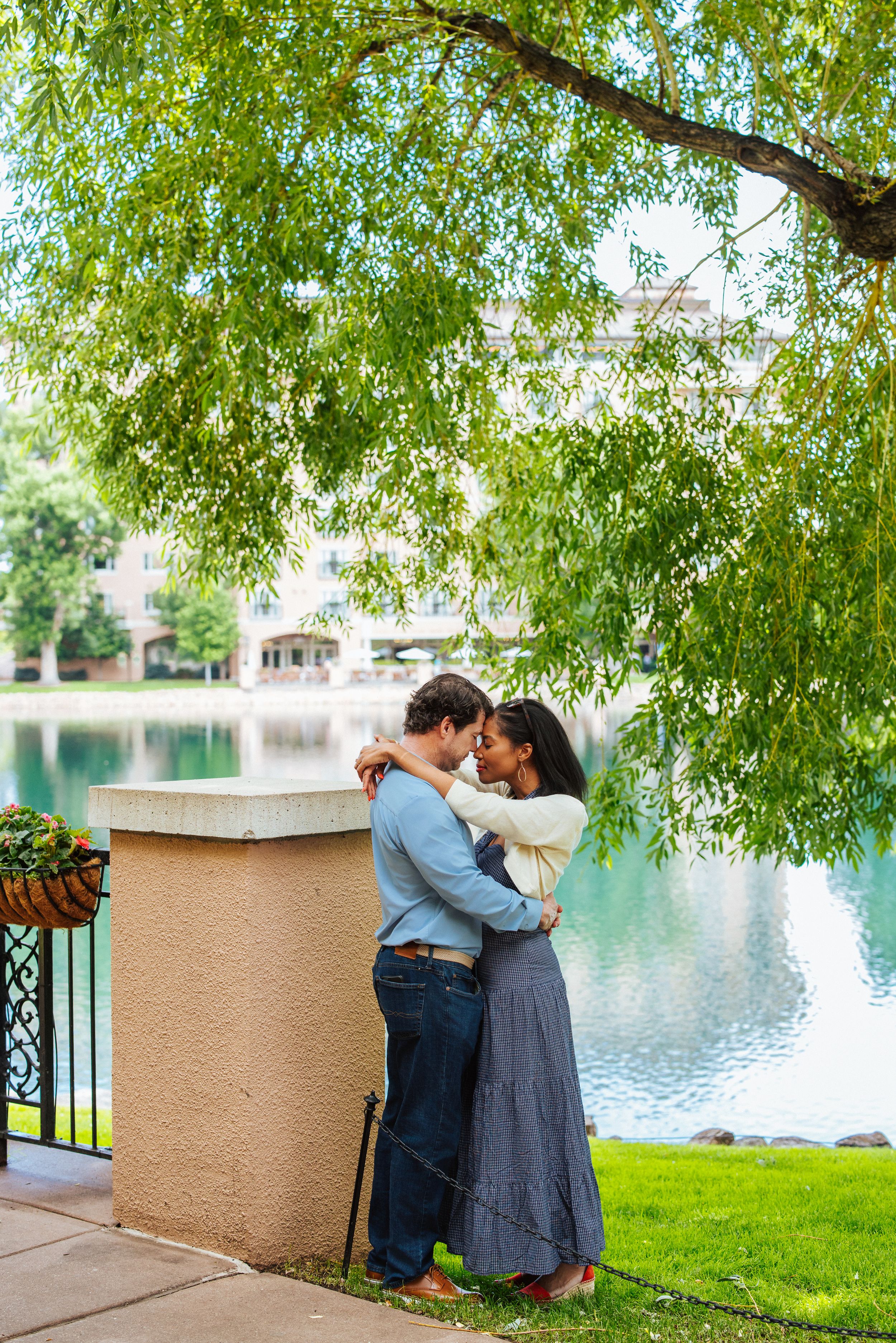 A romantic moment captured by a lake under the cascading branches of a weeping willow tree.
