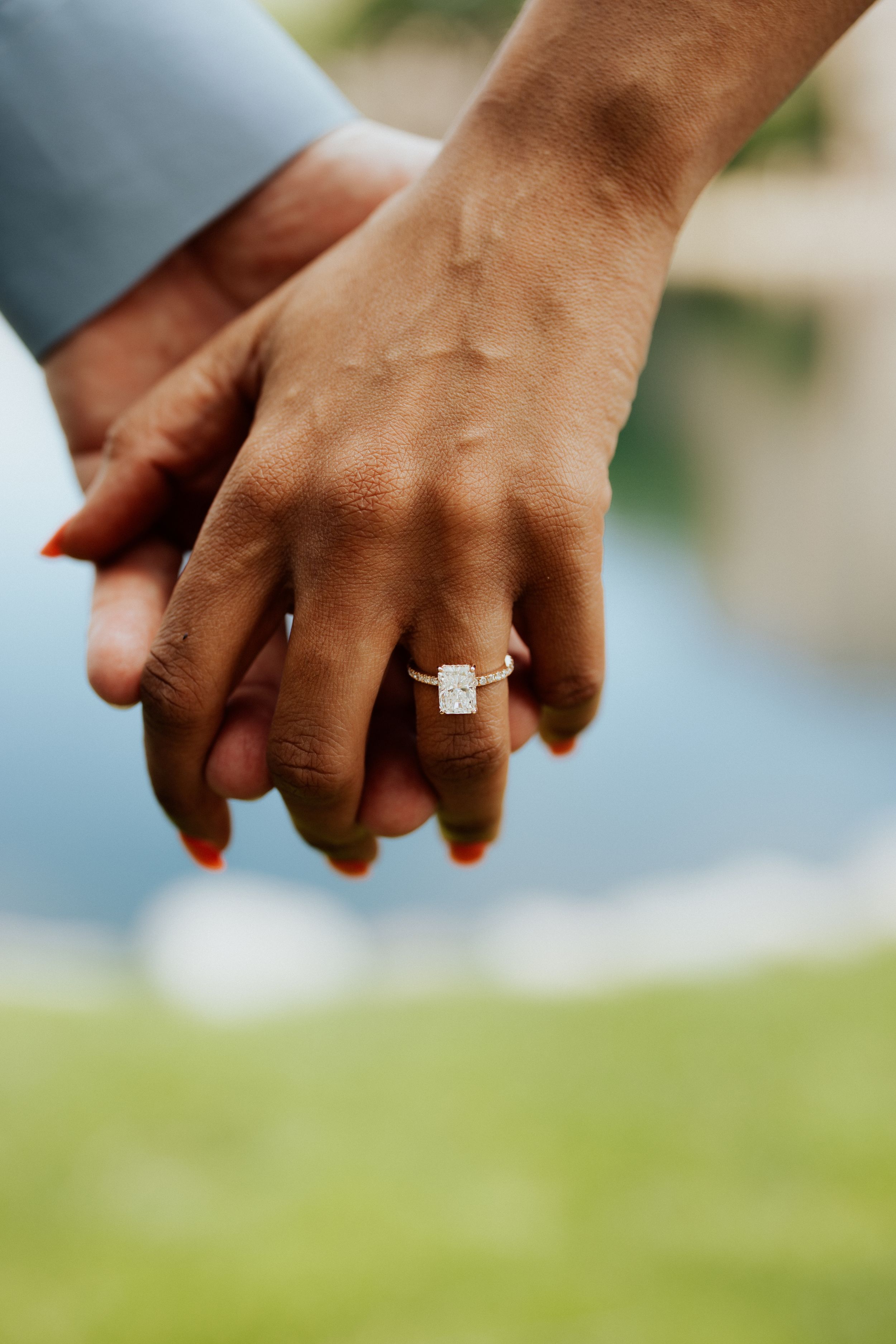 Close-up view of hands with an engagement ring in natural outdoor lighting.