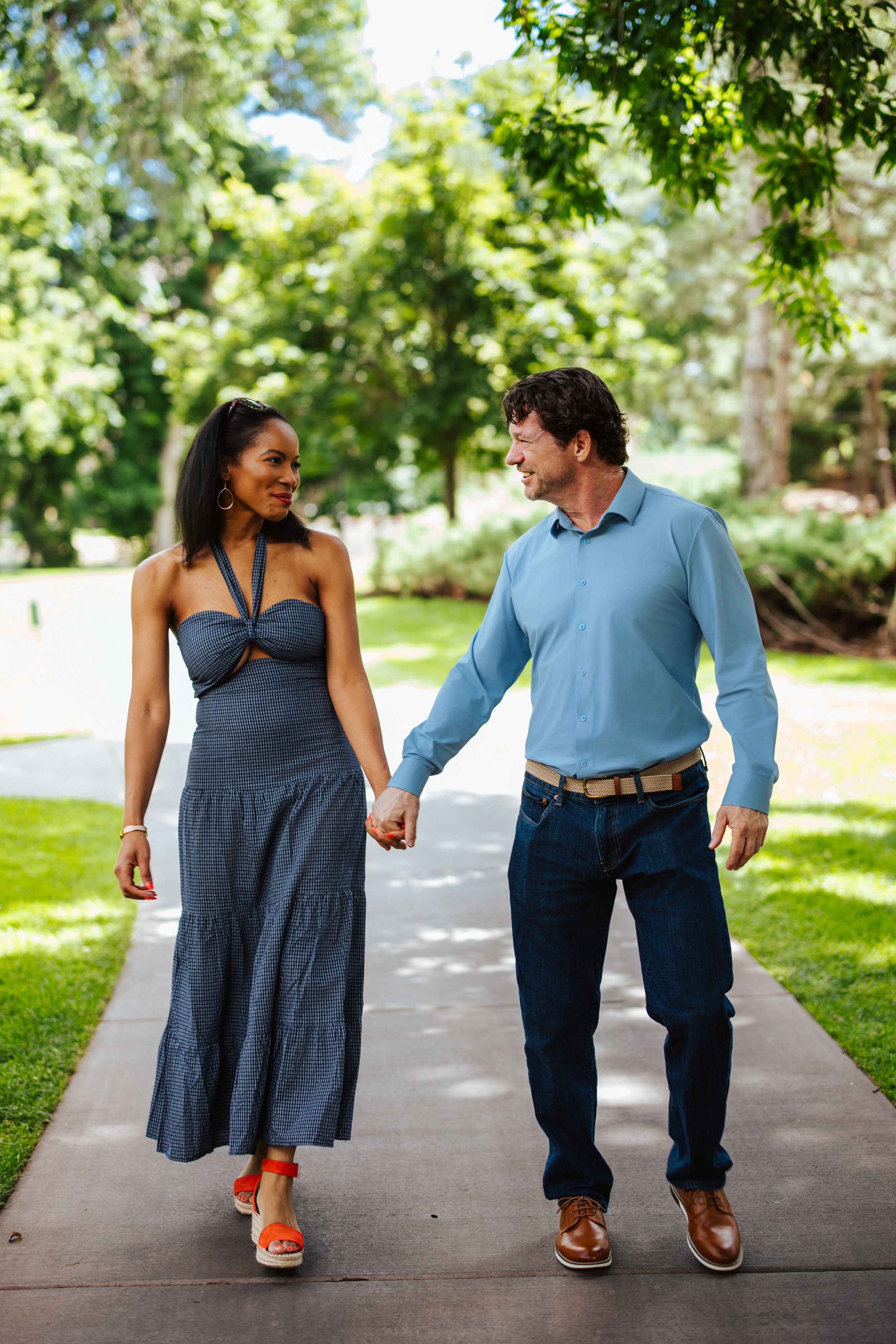 A couple walks together holding hands on a tree-lined path while sharing romantic moments and laughter.
