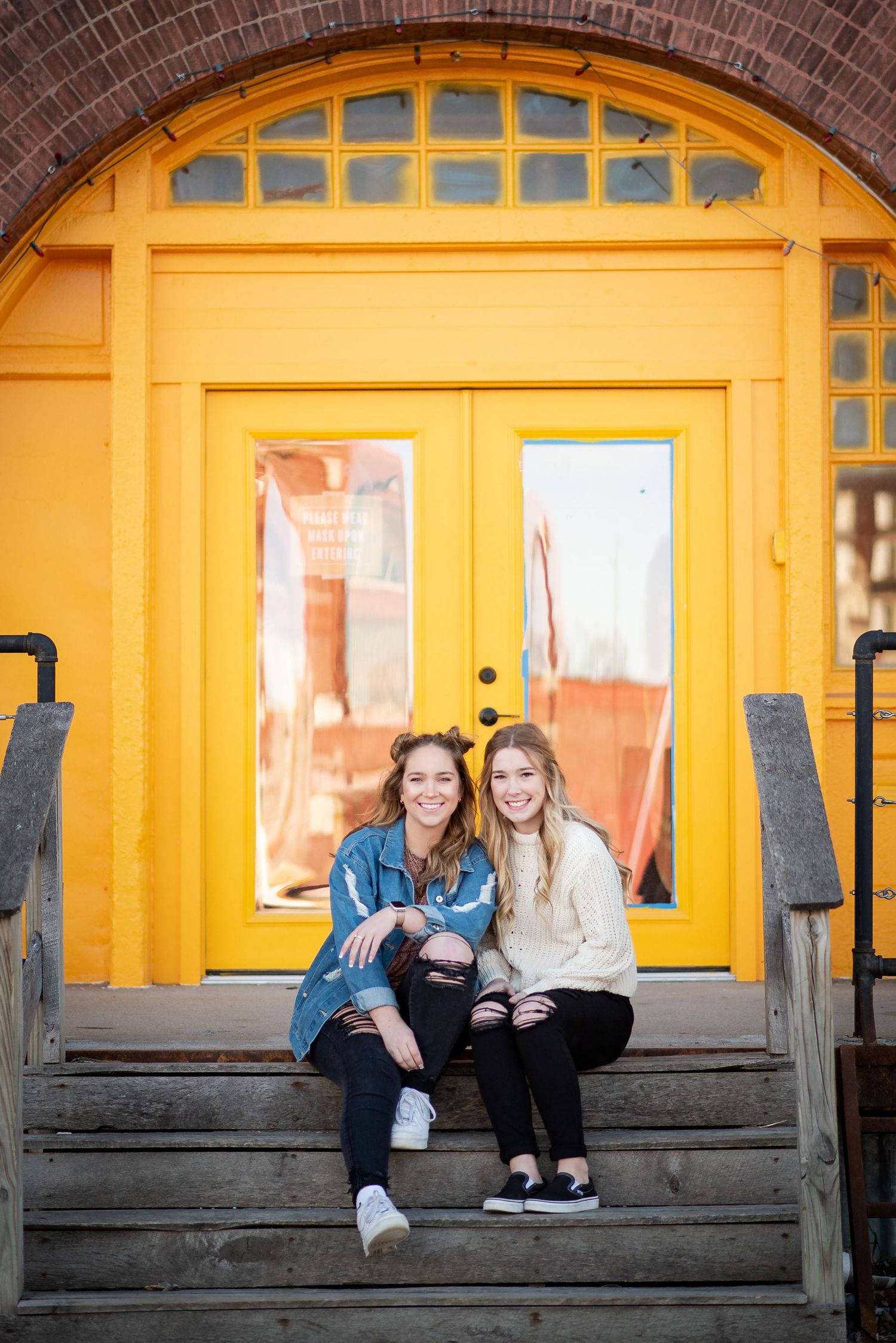 Two smiling young women pose for a piggyback photo under a bridge on a road with yellow lines.