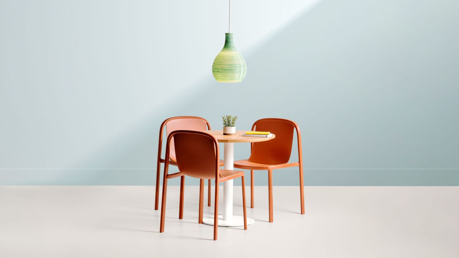 Minimalist dining setup with two orange chairs and small table under green pendant light.