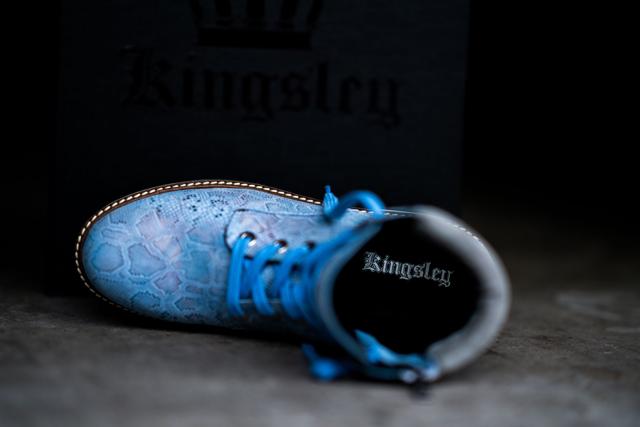 Blue leather boot with bright laces photographed from above against dark background.
