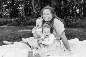 A black and white portrait of a parent and two young children sitting together on a blanket outdoors.