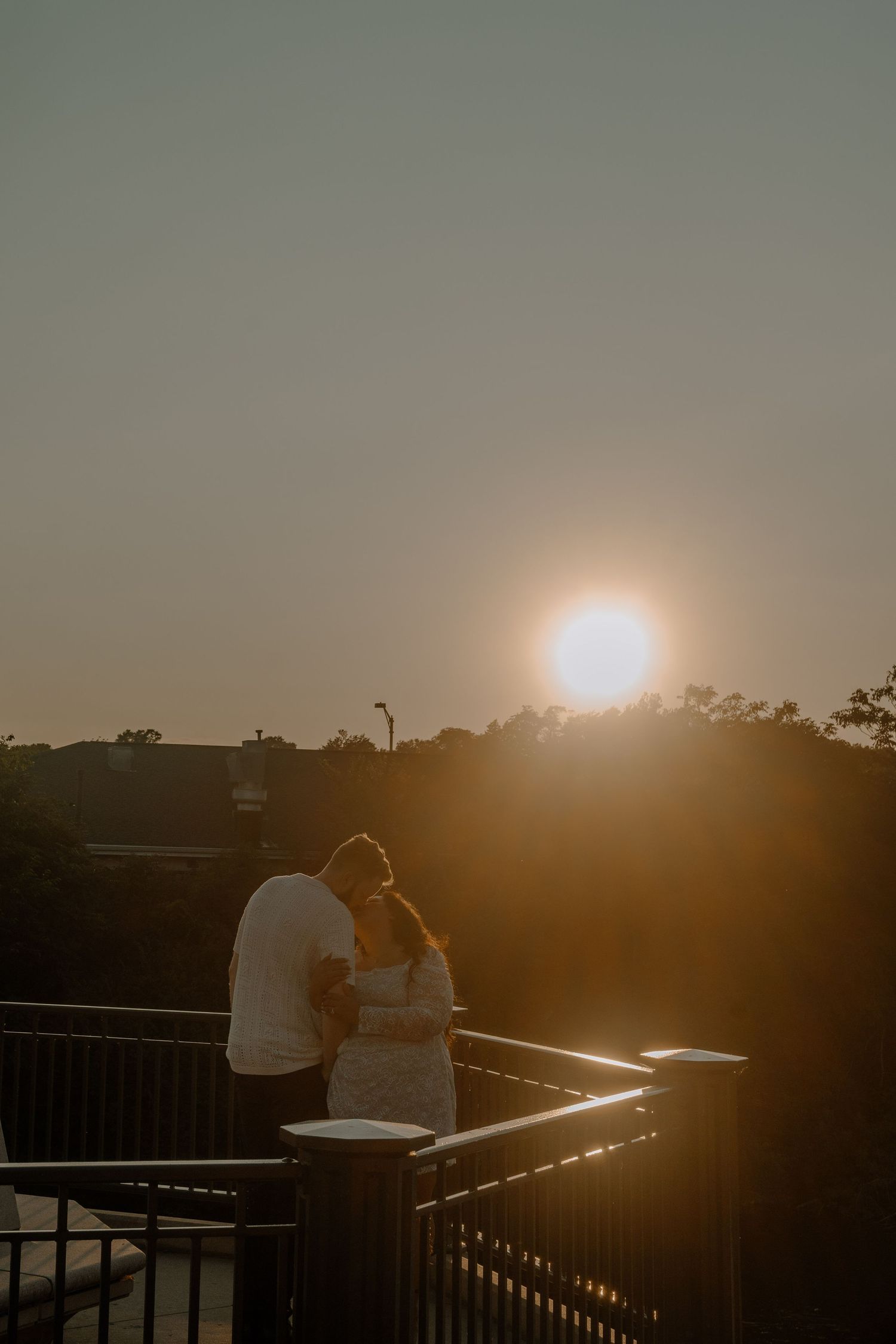 A silhouetted couple stands on a balcony viewing deck against a dramatic golden sunset creating a romantic scene.