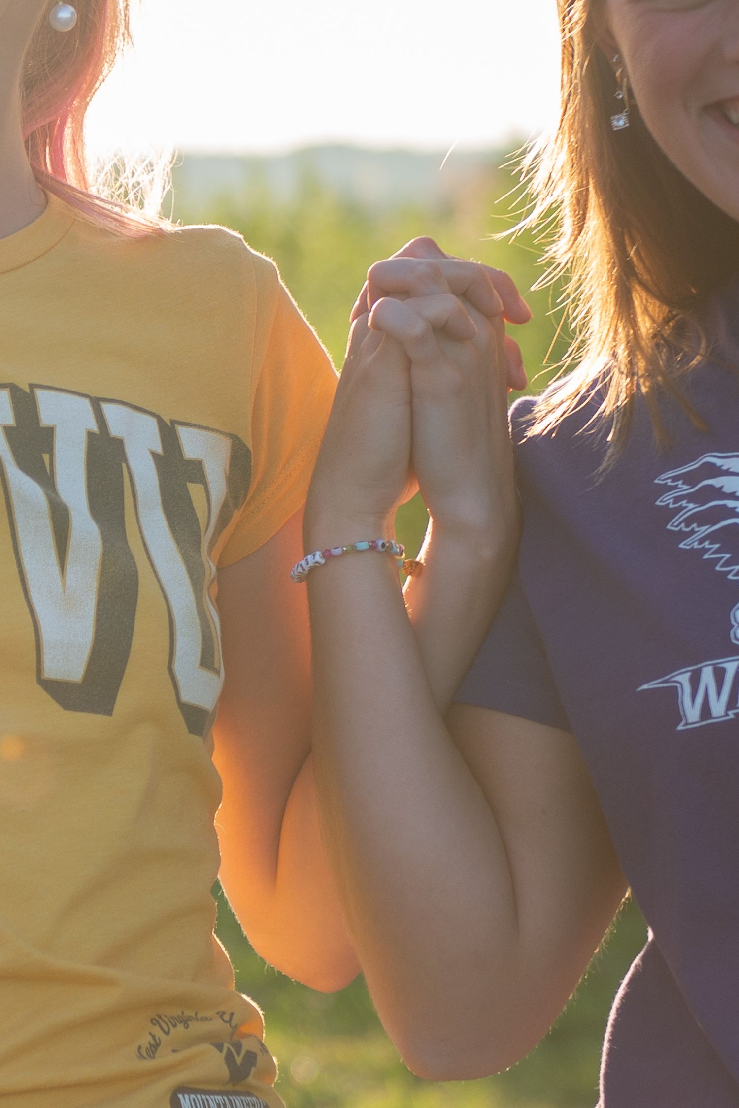 Two people wearing college apparel holding hands together in warm sunset lighting.