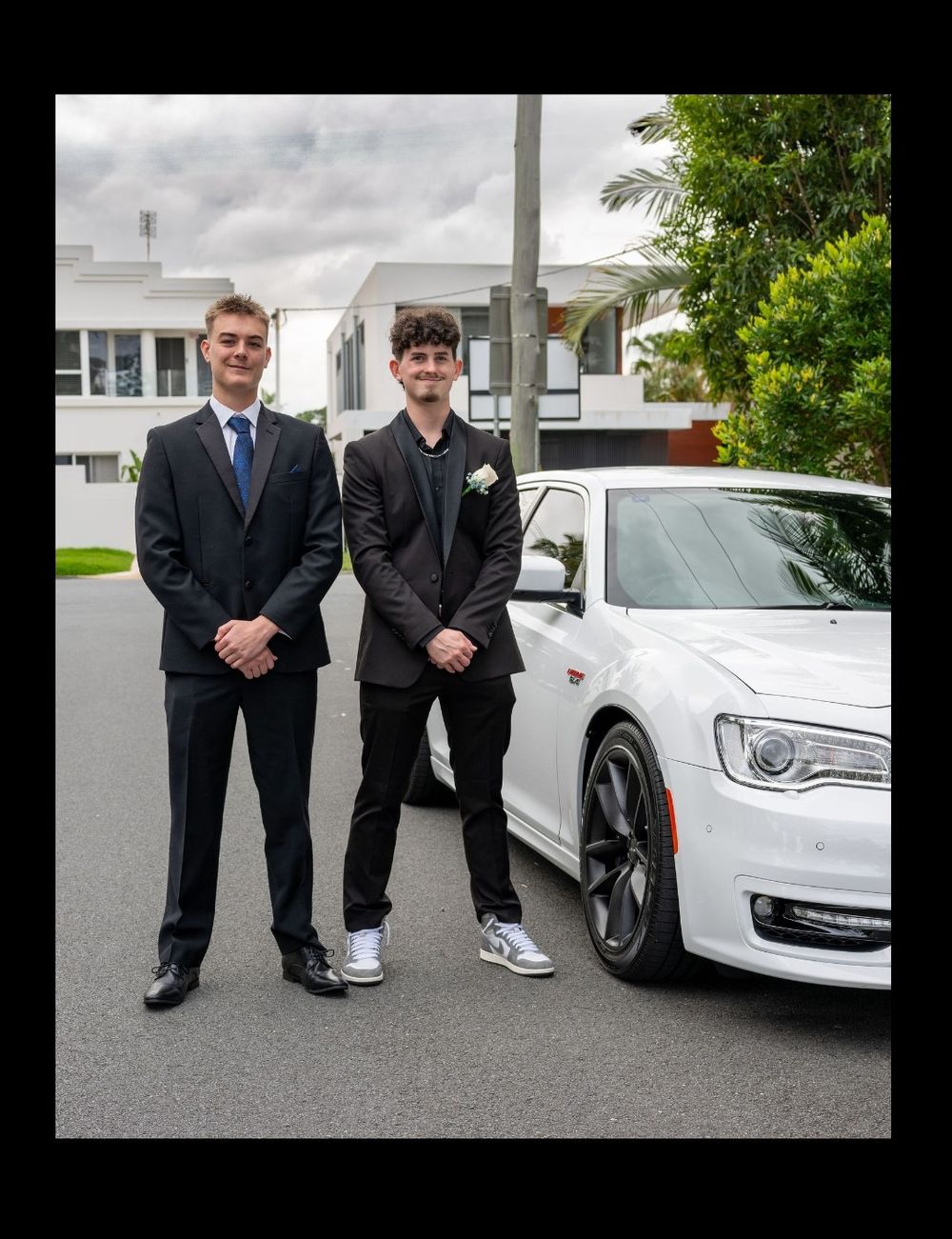 Portrait of two young men in suits standing in front of their formal car
