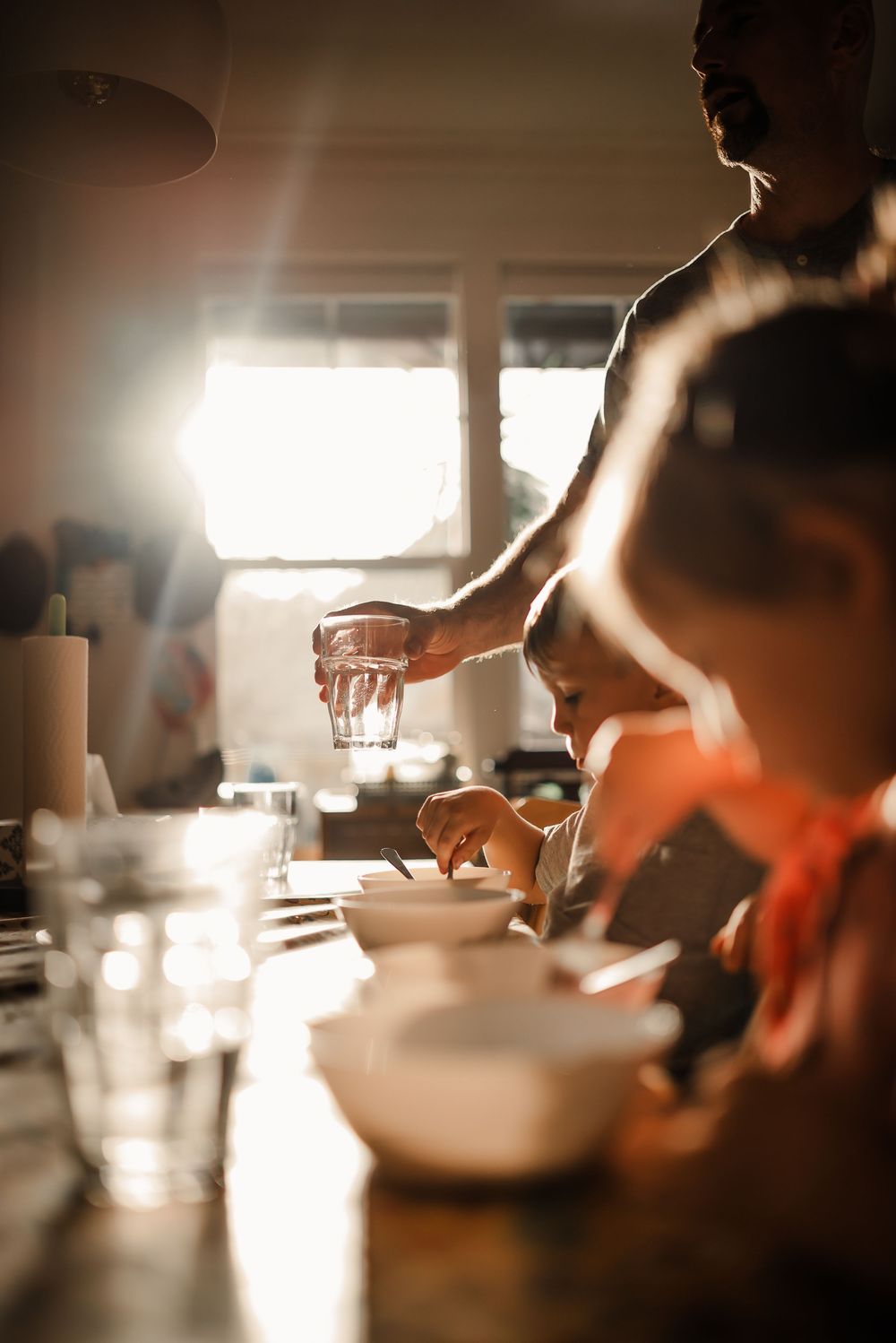 Hands mix ingredients in a white bowl during morning food preparation in warm window light.