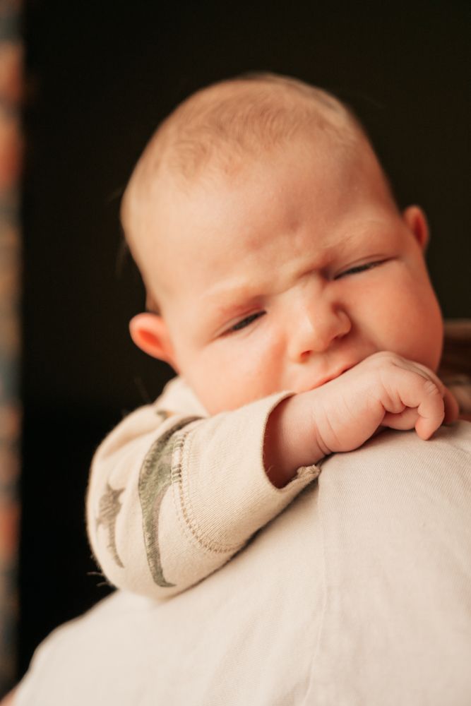 A sleeping baby rests peacefully with their face nestled against a soft white blanket in a tender close-up portrait.