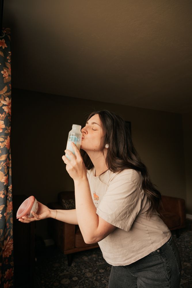 A person in a beige shirt and dark pants sits in a dimly lit room while interacting with a mobile phone.
