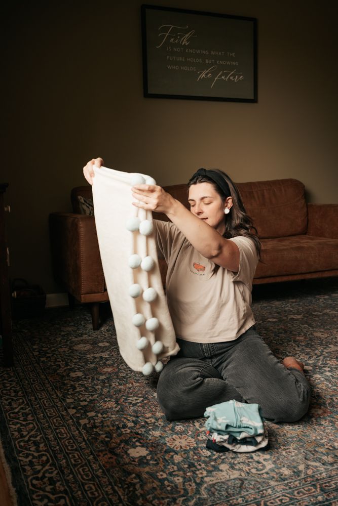 A person sits on a patterned carpet holding a white plush or fabric object while leaning back in a relaxed pose.