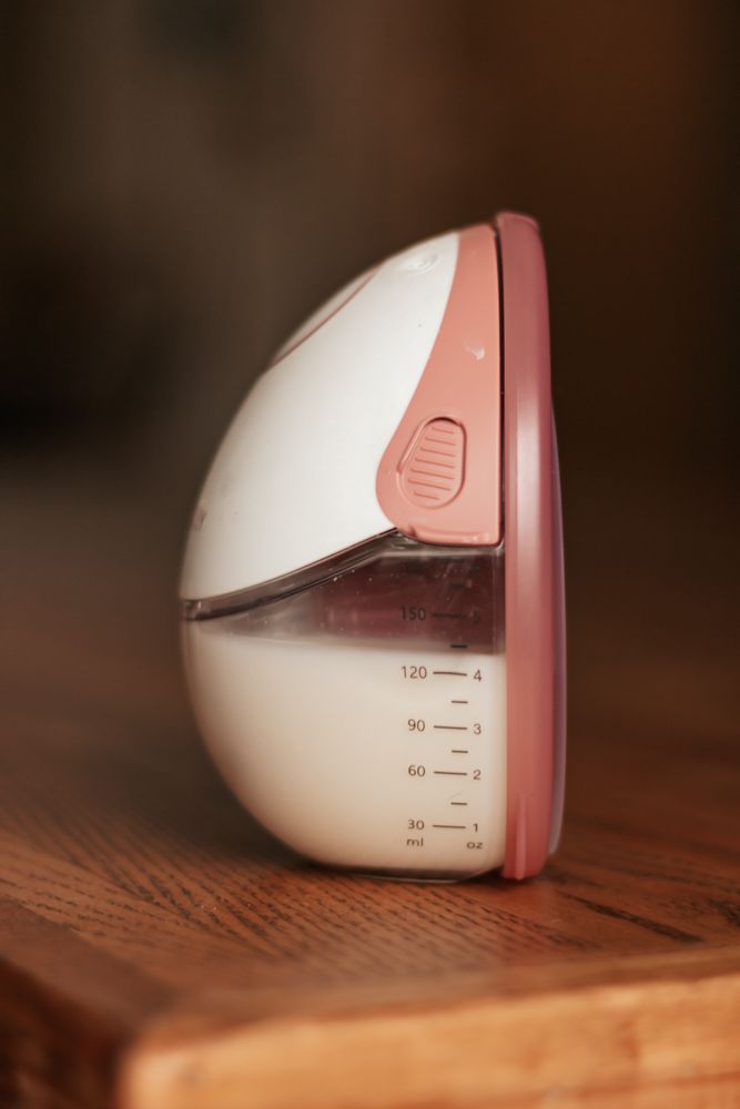 White and pink breast pump device shown from different angles on a wooden surface with measurement markings visible.