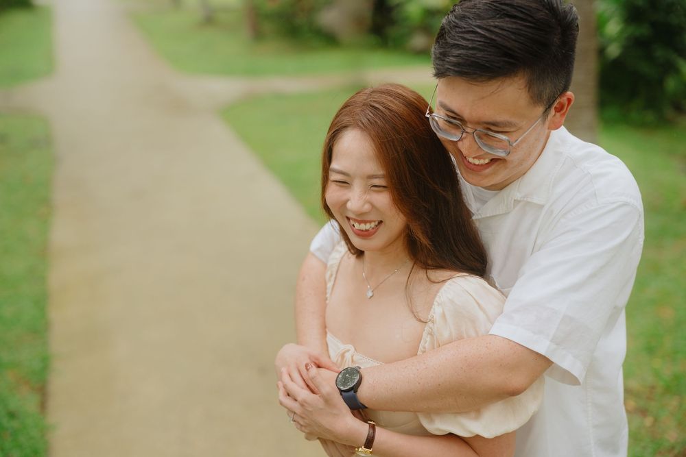 Young couple embraces and laughs together on a garden path with lush greenery in background.