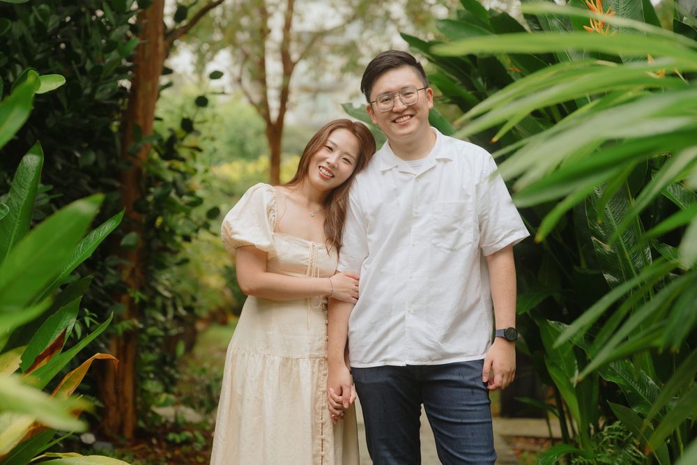 A happy couple poses together outdoors surrounded by lush tropical plants and greenery in a garden setting.