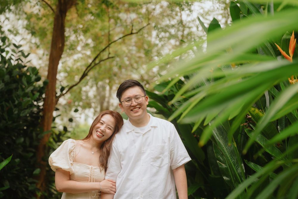 A couple enjoys a romantic moment together in a lush tropical garden setting with green foliage surrounding them.