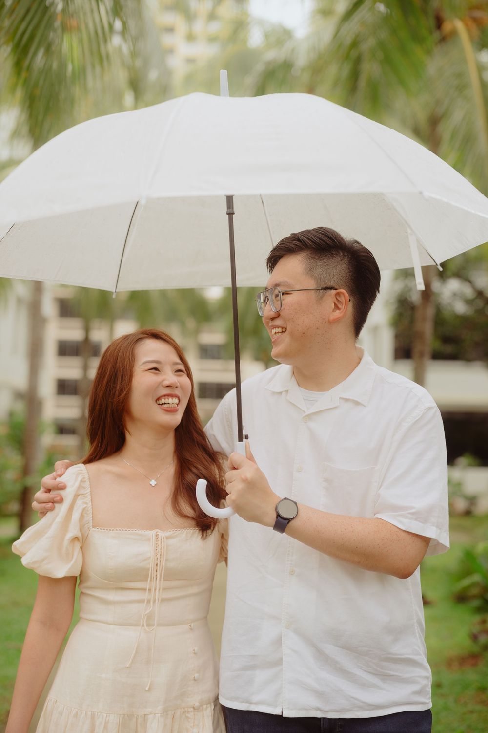 A couple shares a romantic moment under a white umbrella against a backdrop of palm trees.