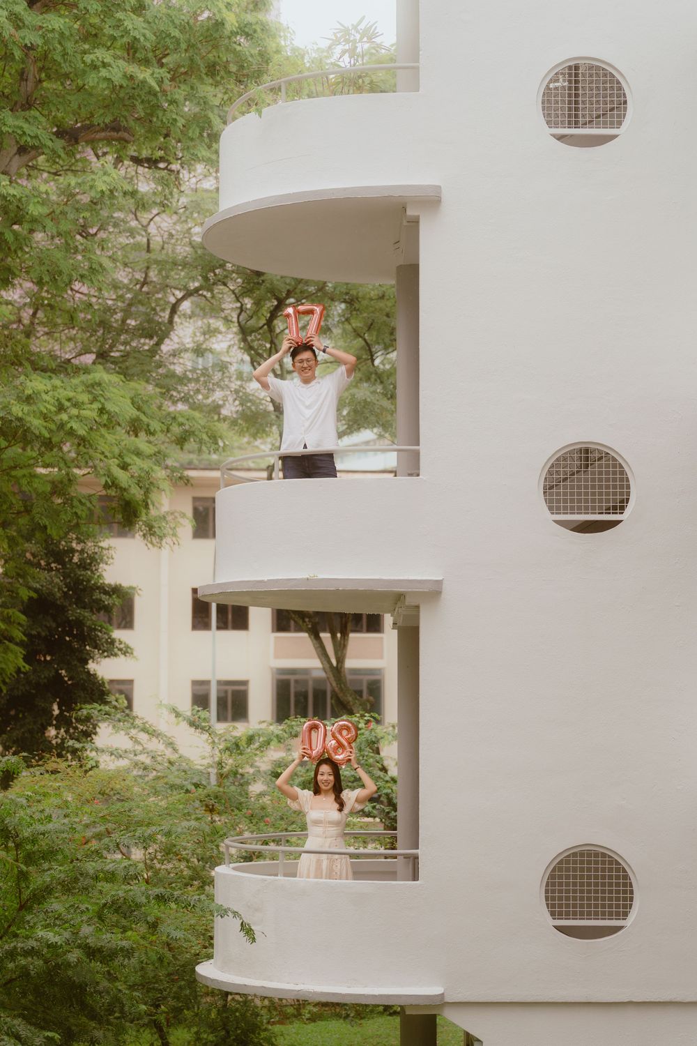 Minimalist white apartment building features curved balconies with circular ventilation details among green foliage.
