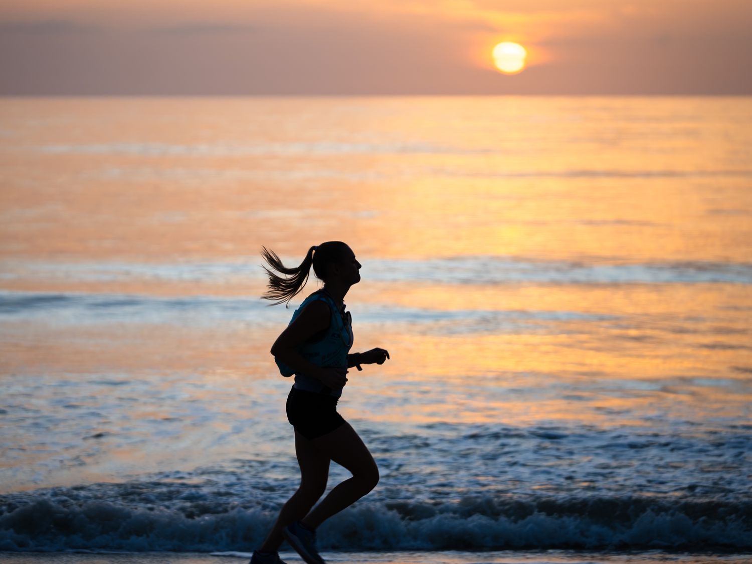 A silhouetted figure leaps between waves at sunset as golden light reflects off the ocean surface behind them.