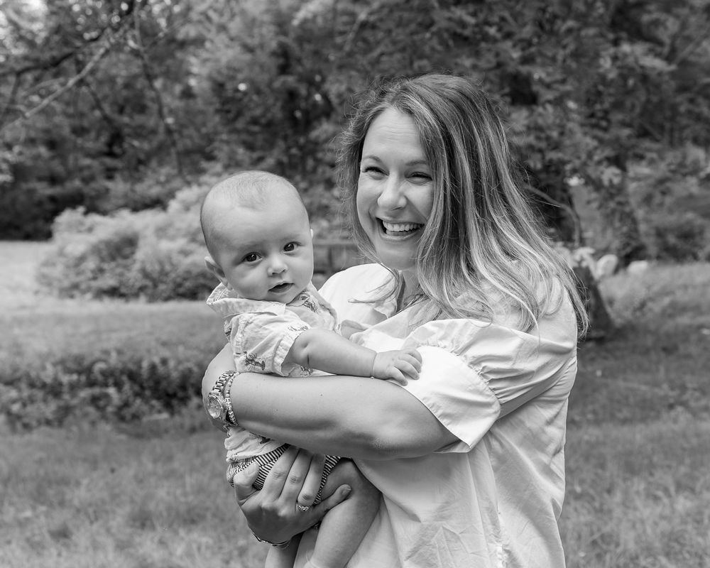 A mom and baby pose candidly on the grounds Wayside Inn Grist Mill during a family photo session in Sudbury, MA with Lisa West Photography.