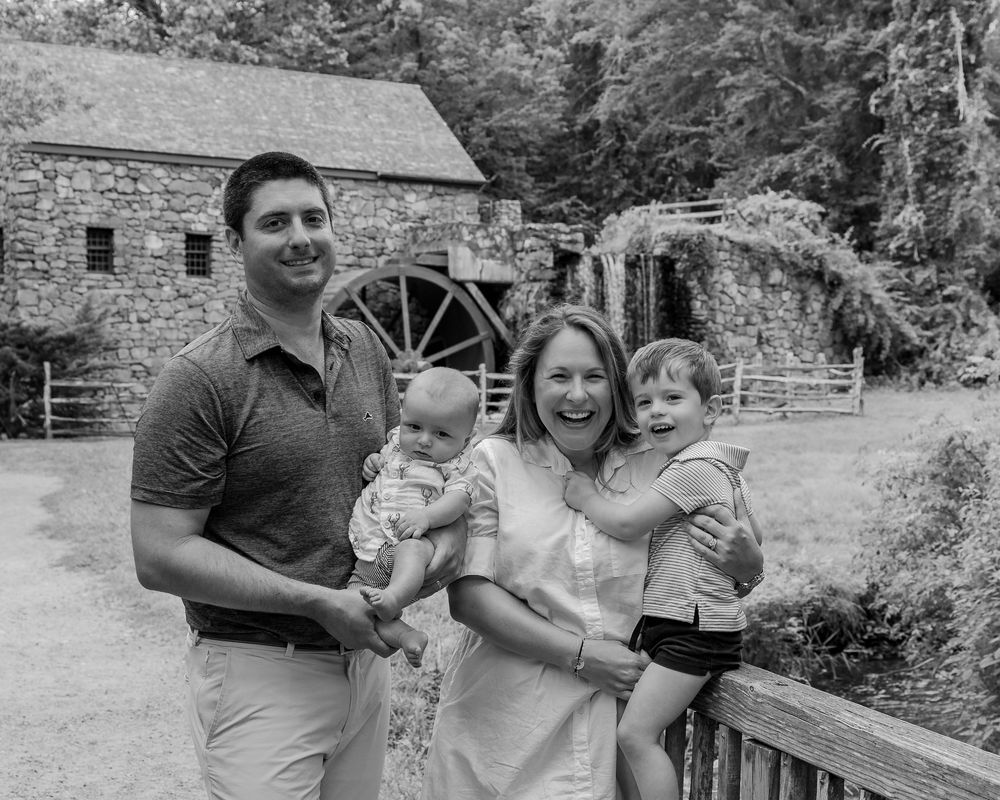 A family photo in B&W in front of the Wayside Inn Grist Mill during a family photo session in Sudbury, MA with Lisa West Photography.