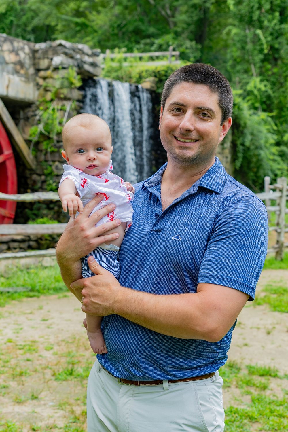 A dad and baby pose on the grounds of Wayside Inn Grist Mill during a family photo session in Sudbury,MA with Lisa West Photography.