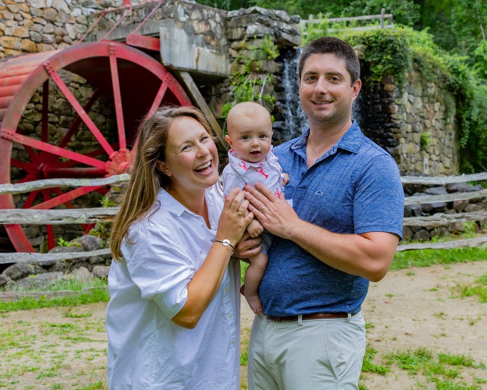 A family poses candidly in front of the Wayside Inn Grist Mill during a family photo session in Sudbury, MA with Lisa West Photography.