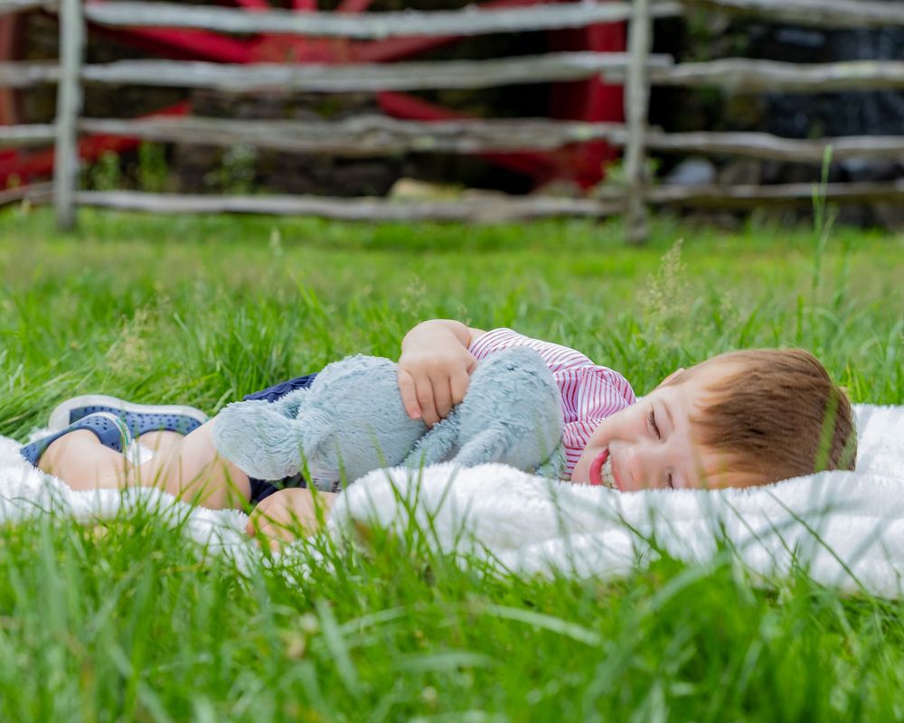 A boy and his lovey pose candidly at the Wayside Inn Grist Mill during a family photo session in Sudbury, MA with Lisa West Photography.