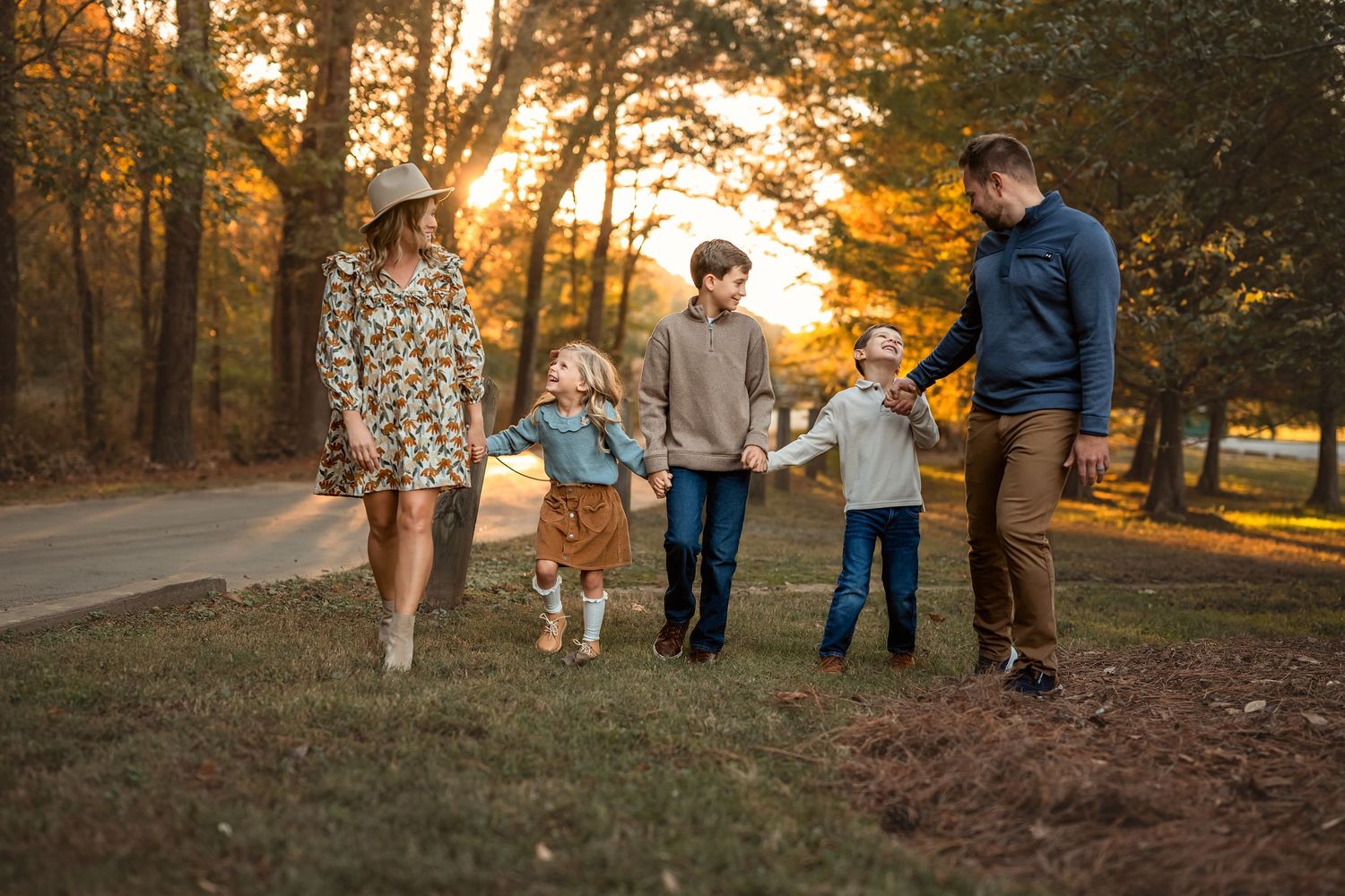 A family of five walks together on a grassy path during golden hour sunset in an autumn forest setting in Atlanta.