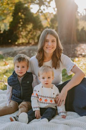A cozy autumn family portrait on a white blanket with sunlight streaming through fall foliage in the background.