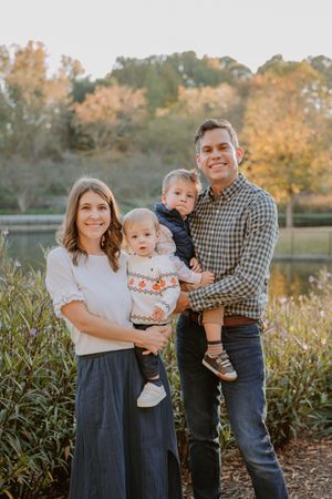 A family poses for an outdoor portrait in front of autumn foliage near a lake.