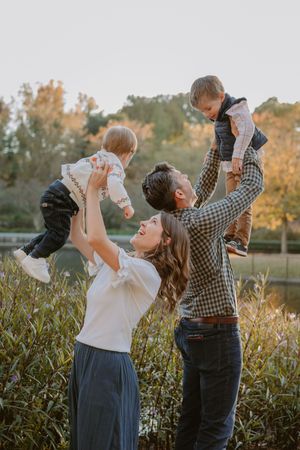 A joyful family moment captured outdoors during golden hour as they playfully lift their children in the air.