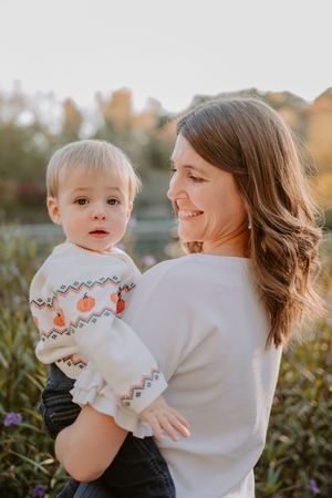 A parent and young toddler share a tender outdoor moment at golden hour wearing matching white sweaters.