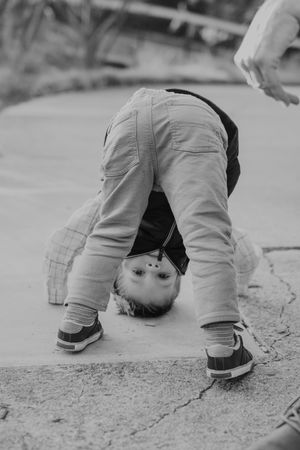A small child bends over backwards in playful pose on pavement in black and white photography.