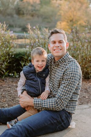 Outdoor family portrait in natural setting with plaid shirt and navy vest against autumn foliage.