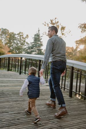 Parent and child walking together on wooden bridge boardwalk at sunset wearing matching navy vests.