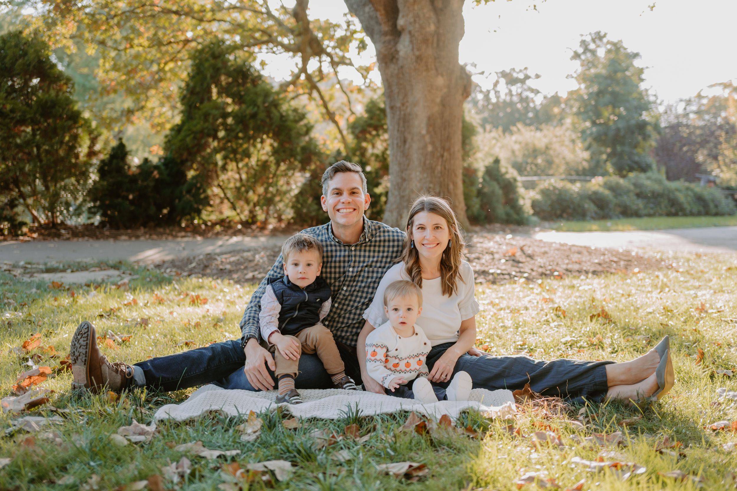 Family enjoys a warm autumn day together relaxing under golden trees in a sunlit park setting.