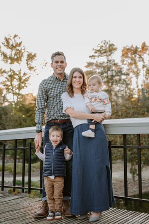 A family stands together on a wooden deck during autumn with trees in the background.