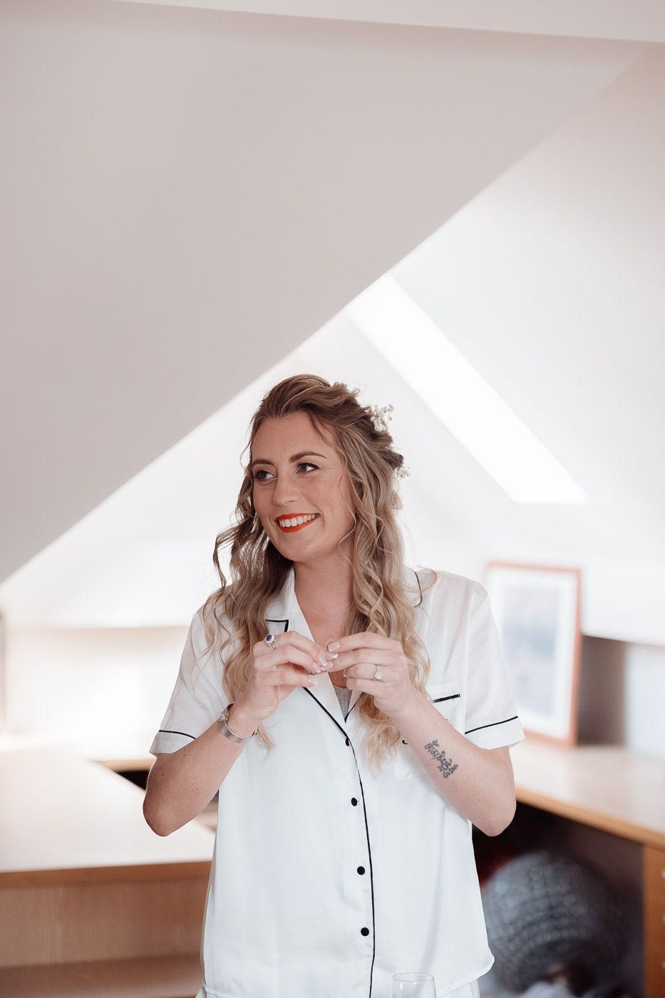 Person wearing white pajamas laughs joyfully in a bright sunlit room while getting ready in the morning.