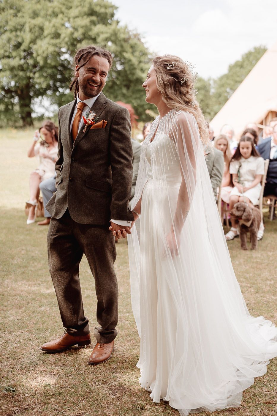 A couple shares a joyful moment during an outdoor wedding ceremony while guests look on in the background.