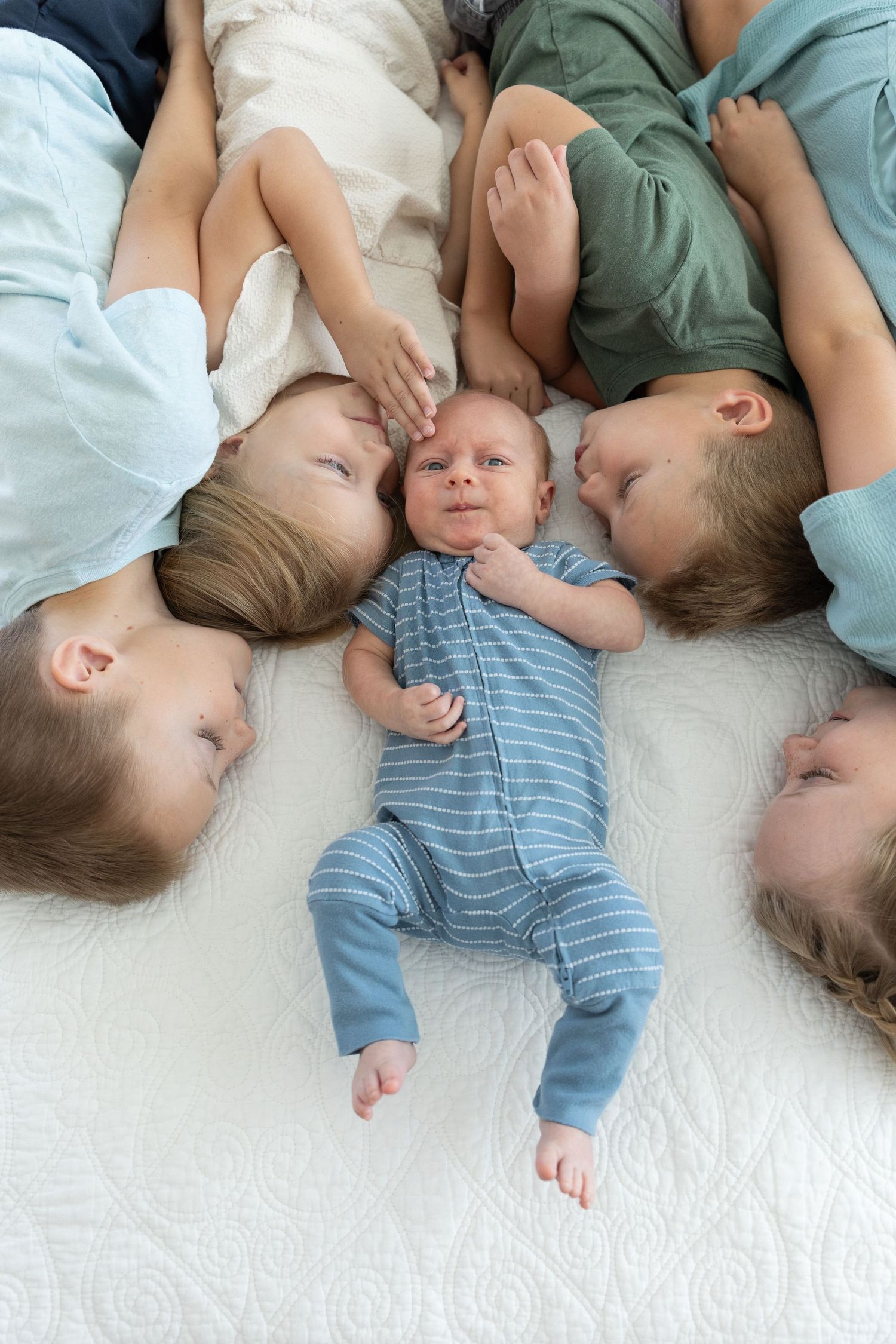 4 children lying on a bed looking at a newborn facing the other way