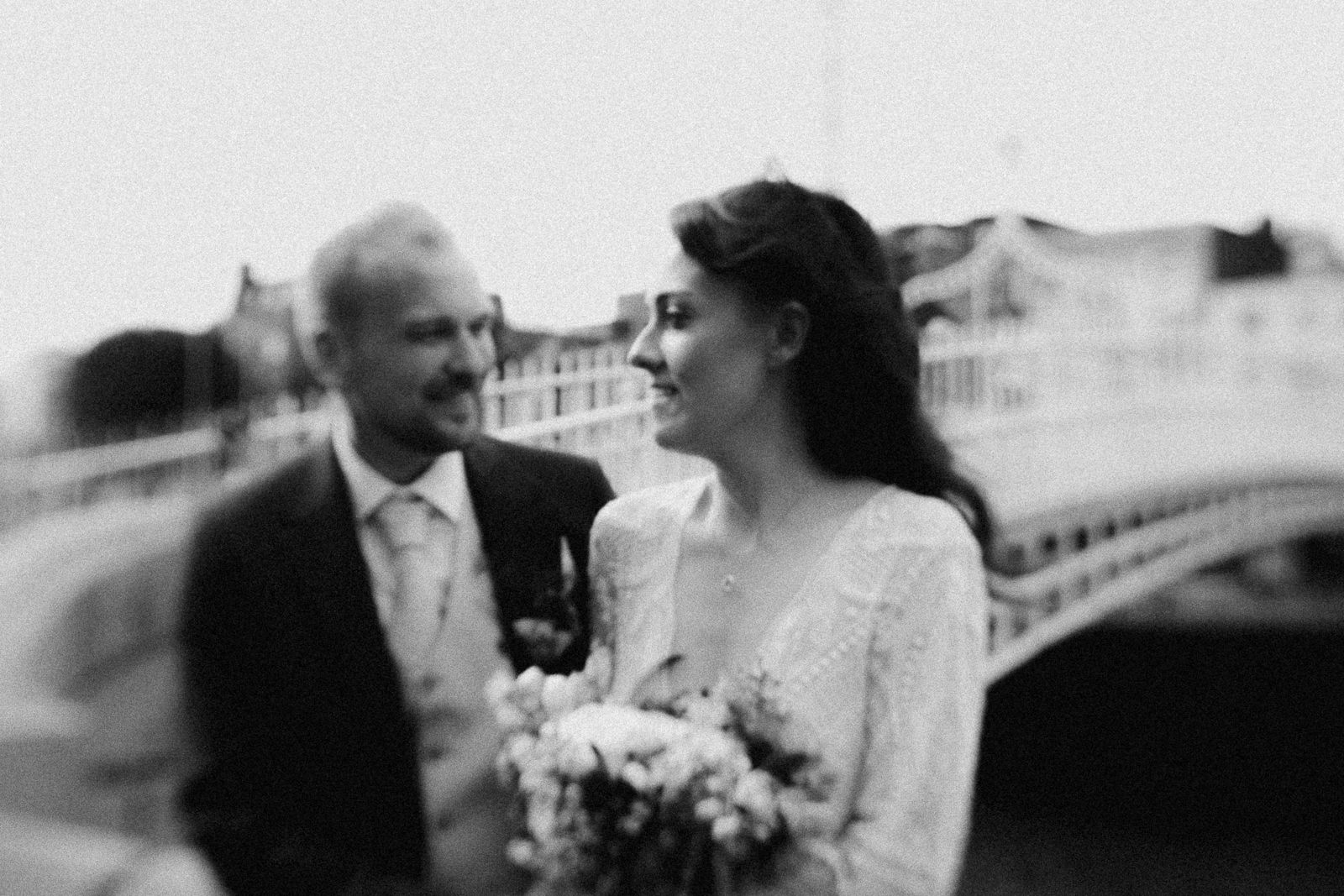 A vintage black and white wedding photograph showing a couple on a bridge.