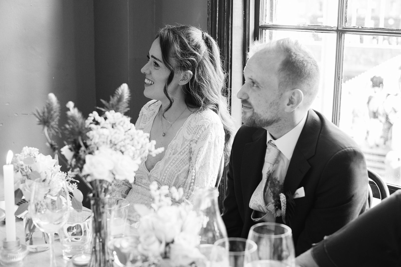 A happy couple shares a candid moment at their wedding reception table with floral centerpieces.