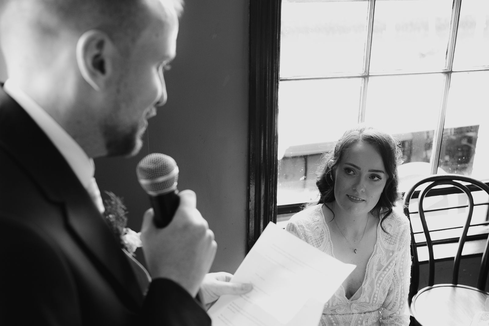 Black and white photo of a wedding reception speech moment at an indoor venue.