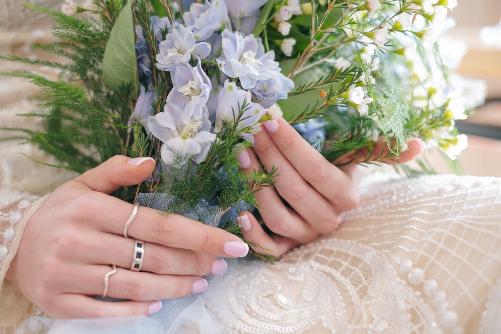 Hands with a wedding ring holding a delicate bouquet of white flowers against a white textured fabric.